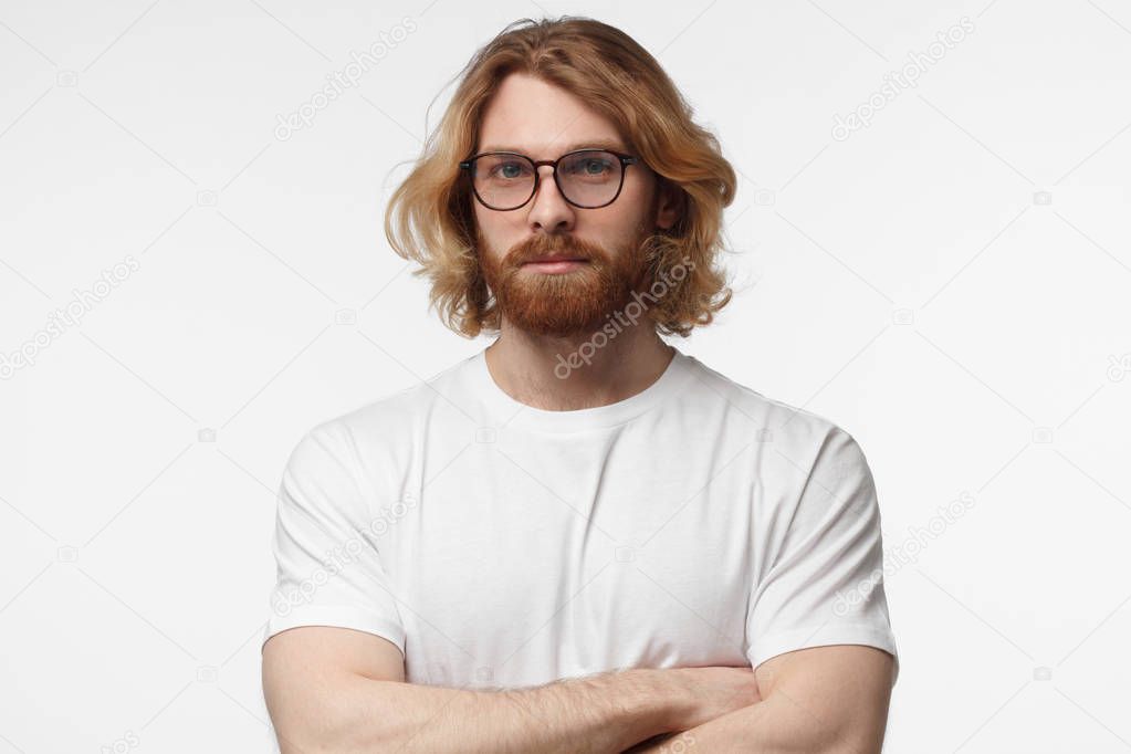 Portrait of smiling handsome bearded man in white tshirt standing with crossed arms isolated on grey background