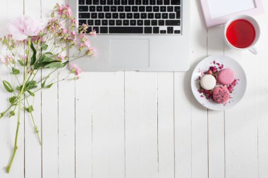Beyaz ahşap masa gri açık dizüstü bilgisayar, siyah klavye ile yalıtılmış yatay görünümünü hafif Pembe çiçek, pembe ve beyaz macarons ve çay, ideal ilham verici çalışma alanı kavramı ile beyaz daire