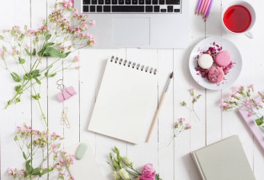 Çalışma tablosu yatay düz üst görünümü gri açık laptop ile beyaz boyalı, pembe çiçek tomurcukları ve yaprakları, renkli kalemler ve macarons ve bahar defter Merkezi'nde boya fırçası ile dağınık