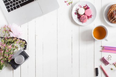 Yatay düz üst görünümü ile açık metal laptop, pasta, çay bardağı ve yaratıcı çalışma için ileti örneği ile çevrili çiçeklerle süslenmiş beyaz masa boş alan Merkezi reklam için
