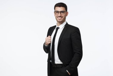 Siyah takım elbise, beyaz gömlek ve kravat dikkatle gözlüklerle bakıyor ve olumlu ve güvenle gülümseyen gri arka plan üzerinde izole varoluş yakışıklı beyaz adam portresi giymiş