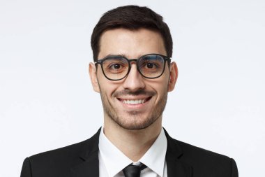 Kendinden emin ve gülümseyen dostu arıyorum genç yakışıklı Avrupa iş adamı gözlük resimde izole üzerinde gri arka plan giyen siyah resmi takım elbise, beyaz gömlek ve kravat, closeup headshot