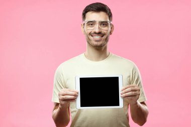 Portre fotoğraf tablet boş ekran, boşaltmak için reklam apps, mal veya hizmet ile tutarak pembe tişört ve plastik gözlük, izole yakışıklı Avrupa gencin