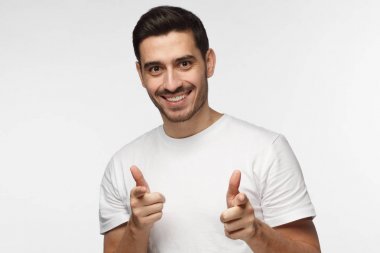Yakışıklı Avrupa adam gri arka plan açık ağız ile mutlu bir şekilde gülümseyerek ve kamera iki eliyle sanki onların çevirmek olduğunu söyleyerek işaret eden beyaz T-shirt giyen izole portre resmi