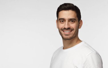 Portre fotoğraf genç yakışıklı Avrupa adam gülümsüyor, boşaltmak için fotoğrafın sol tarafında reklam resim sağ tarafındaki beyaz casual T-shirt giymiş resimde izole üzerinde gri arka plan