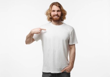 Genç yakışıklı sakallı erkek ile beyaz arka plan üzerinde izole uzun sarı saçlar varoluş portresi parmak sağ elin, boşaltmak için reklam göstererek beyaz boş T-shirt giymiş