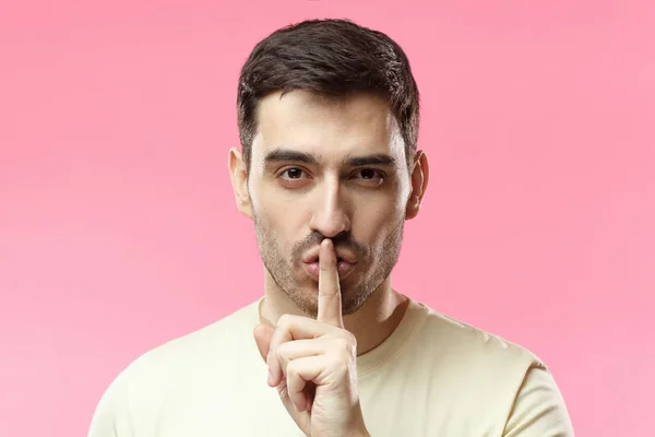 Closeup picture of young handsome Caucasian guy pictured isolated on pink background pressing finger to lips asking to keep silent, not willing to tell everyone about limited chance or unusual offer — Stock Photo, Image