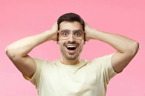 Inomhus foto av unga stiliga kaukasiska manlig isolerad på rosa bakgrund klädda i casual T-shirt, bär transparenta glasögon visar intensiv förvåning med något lovande och positiva — Stockfoto