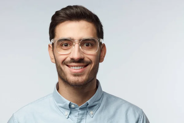 Portret zbliżenie młody przystojny kaukaski mężczyzna na białym tle na szarym tle sobie przezroczyste okulary ochronne i dorywczo koszulę, uśmiechając się szczęśliwie patrząc prosto w obiektyw kamery, uczucie zawartości — Zdjęcie stockowe