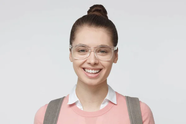 头像年轻的欧洲白种女人的照片在灰色背景下, 身着休闲粉红色套衫和戴着塑料透明眼镜显示友好和乐观与微笑 — 图库照片
