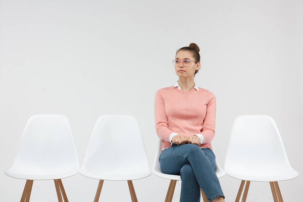  Confident successful young woman wearing stylish pink sweater and glasses holding digital tablet while waiting for appointment, sitting on chair 