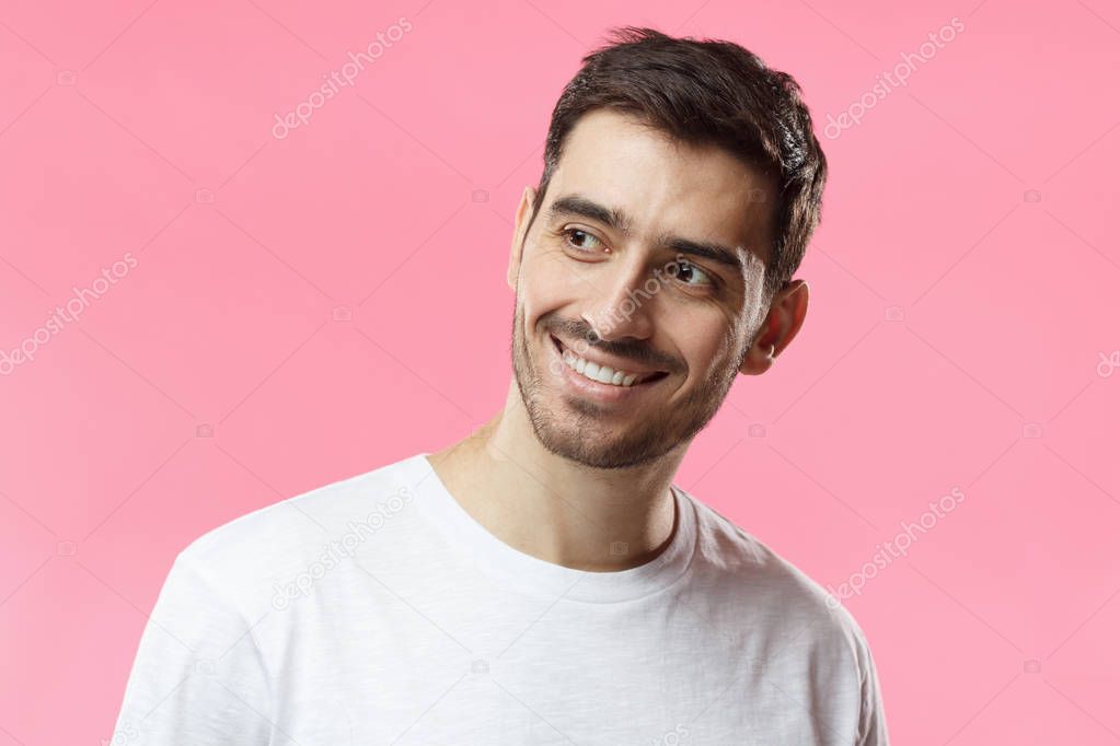 Closeup headshot of young European Caucasian man pictured isolated on pink background smiling happily, looking aside as if waiting for mate or girlfriend, feeling positive, relaxed and joyful