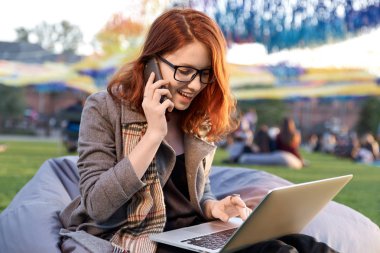 Üniversitede mutlu beyaz kadın bahar günü güzel bir şehir parkta otururken net-kitap üzerinde klavye sınavları için hazırlık için taşınabilir dizüstü bilgisayar kullanan genç gülümseyen kadın öğrenci