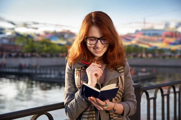 Lächelndes fröhliches Mädchen notiert in ein Notizbuch und plant, wie — Stockfoto