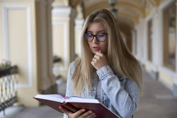 Giovane bella studentessa con i capelli lunghi pensierosamente la lettura di un — Foto Stock