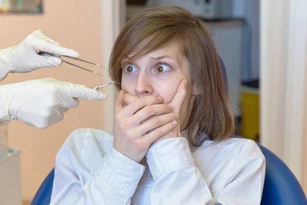 Młoda kobieta jest w szoku przez strach i przerażenie instrumentów dentystycznych, które patrzy na z jej oczy szeroko otwarte. — Zdjęcie stockowe