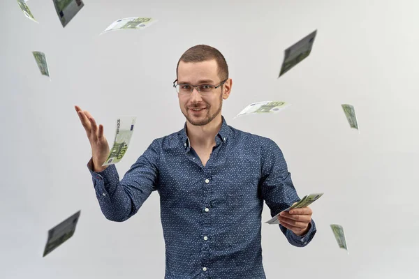a successful young man in shirt and glasses holding a wad of cash and throws it up around yourself