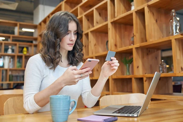 bir kafede bir masada oturan bir dizüstü smartphone ile modern genç kadın kız online sipariş için ödeme yapar.