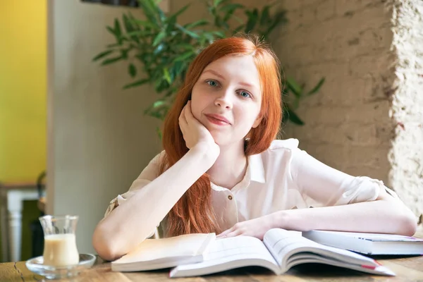 Junge attraktive Studentin mit weißer Haut und langen roten Haaren liest Bücher, studiert, umgeben von Büchern — Stockfoto