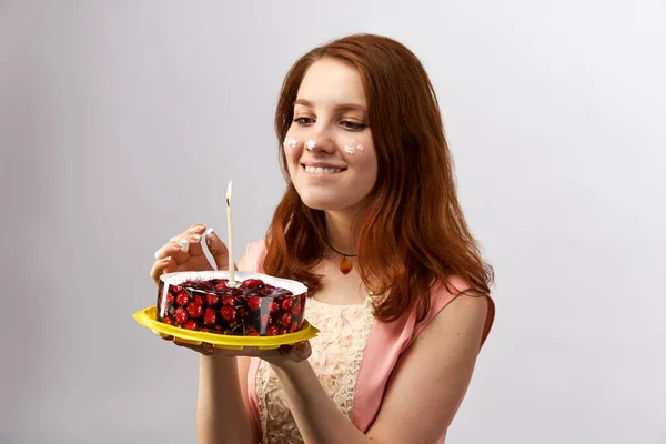 Joven atractiva chica pelirroja sosteniendo un pastel con vela y pide un deseo en el cumpleaños . —  Fotos de Stock