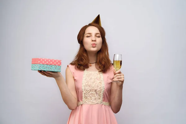 Piękna młoda dziewczyna z długimi rudymi włosami trzyma kieliszek szampana i pole prezent. — Zdjęcie stockowe