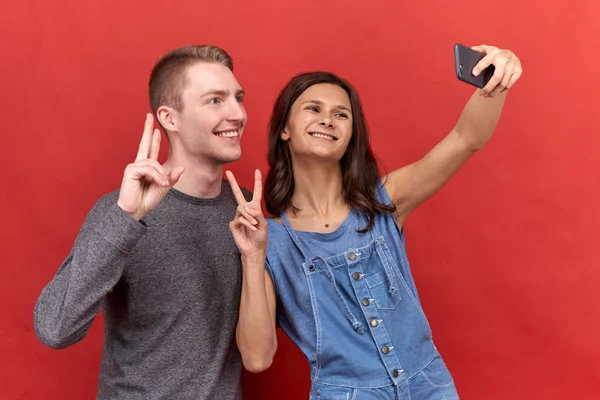 Para två vänner gör en selfie på telefon, isolerade leende och titta gärna in kameran på bakgrund. — Stockfoto