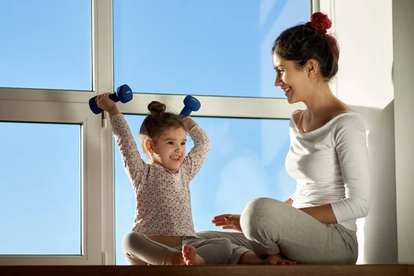 Küçük kız çocuk mutlu bir dumbbell ve gülümsüyor, annesine başarılarından gösterilen yükseltir.
