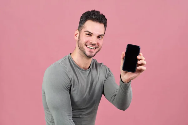 Atlético atractivo hombre en apretado camiseta amplia sonríe felizmente, sosteniendo en la mano smartphone con pantalla convertida en cámara . —  Fotos de Stock