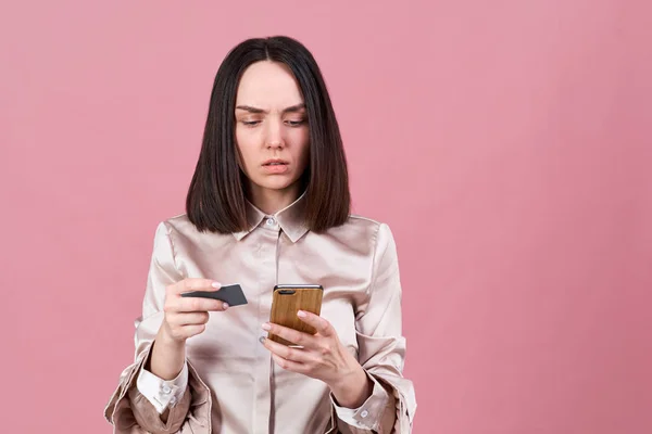Snygg ung brunett kvinna med en allvarlig koncentrerat uttryck använder kort för att betala för köp på Internet med hjälp av en smartphone — Stockfoto
