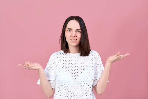 Arg upprörd ung brunett kvinna argt kastar upp händerna framför henne och rynkar pannan. Stor Studio porträtt på rosa bakgrund — Stockfoto