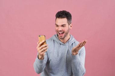 Sportif genç adam yeni mobil uygulaması ve heyecanla gülümseyen ve seyir telefon ellerini sallayarak hakkında heyecanlı olduğunu. 