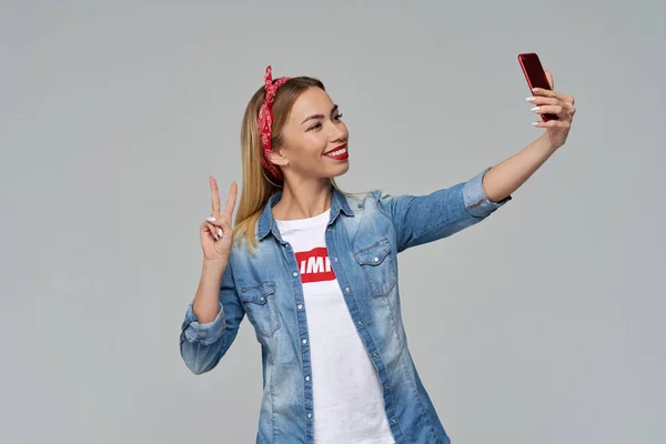 Unga hipster kvinna tar selfie på smartphone, ler brett och visar tecken på seger och fred. — Stockfoto