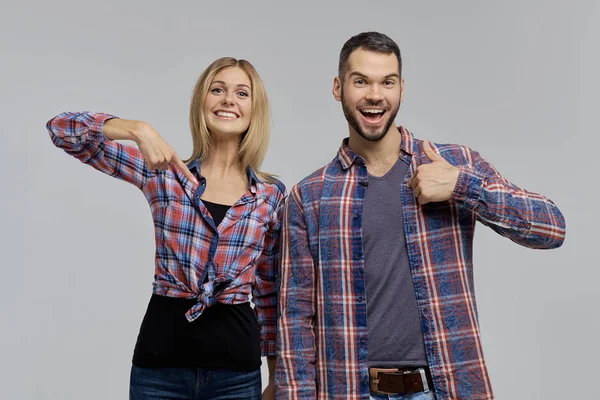 Una joven pareja con camisas a cuadros y vaqueros - un hombre y una mujer se señalan a sí mismos y señalan con el dedo hacia arriba . — Foto de Stock