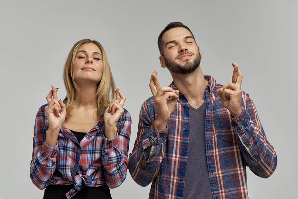 Pareja joven en camisas a cuadros cerró los ojos y sonrió, los dedos cruzados. Concepto de sueños, deseos y esperanzas de victoria — Foto de Stock