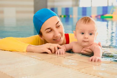 Küçük anne ve oğlu havuzda yüzme dersi veriyor.