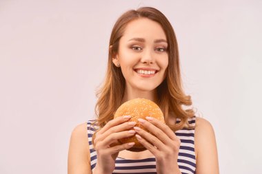 Kız hafifçe kar beyazı gülüşü lezzetli hamburgerler yiyor.