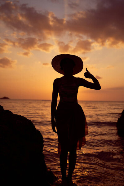 Contrast silhouette young slender woman against background of Sunny sunset, sea sandy beach. Warm evening tones. Lady walking on beach in sunset, vacation city Patong Phuket country Thailand, vertical