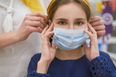 Anne kızının koruyucu maske takmasına yardım ediyor.