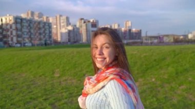 Kadın döndü, profili, nazik gülümsemesi, kameraya baktı, yarım yamalak, güzel gözlü. Güneşli bir videoda kadın gün batımında parkta yürürken görülüyor. Orta yaşlı esmer kız, rüzgar uzun siyah saçlar savuruyor.