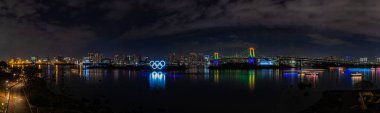 Tokyo Körfezi 'nin panorama resmi, aydınlatılmış Gökkuşağı Köprüsü, ve aydınlatılmış Olimpiyat Halkaları, geceleri.