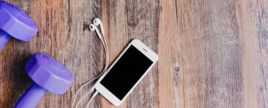 Ahşap arka plan, metin kopyalama yeri olan Web sitesi header tasarımı için fotoğraf afiş üzerinde smartphone, earphones ve dumbbell ile düz yatıyordu fitness öğelerin en iyi görünümü 