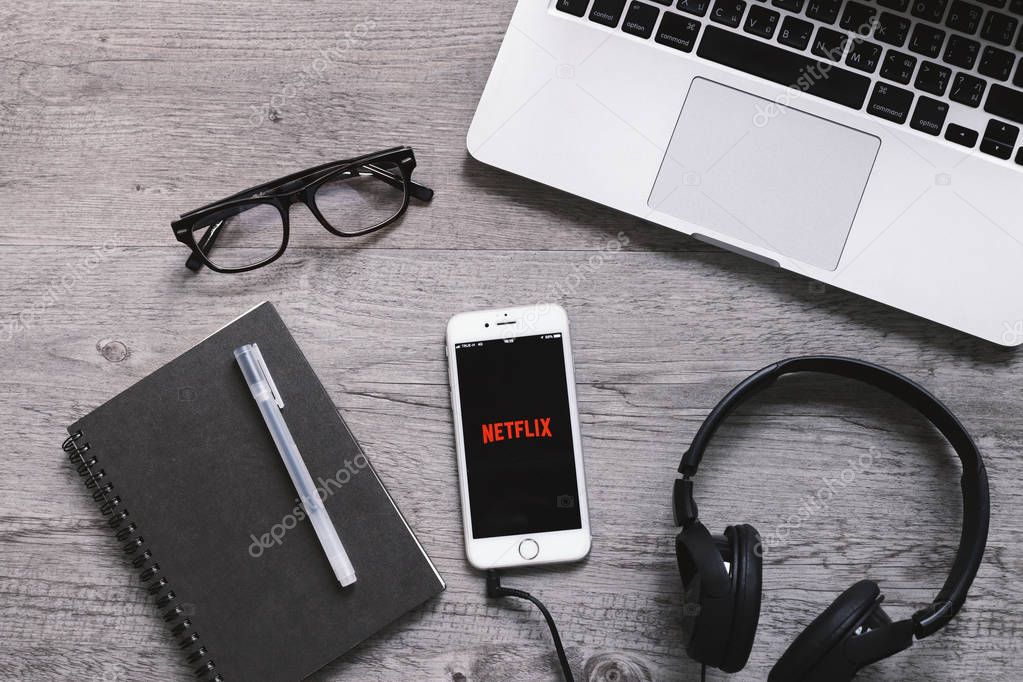 BANGKOK, THAILAND - April 28, 2018 : Top view of Netflix app icon on iphone screen with headphone and laptop. Netflix is an international leading subscription service for watching movies and TV series.