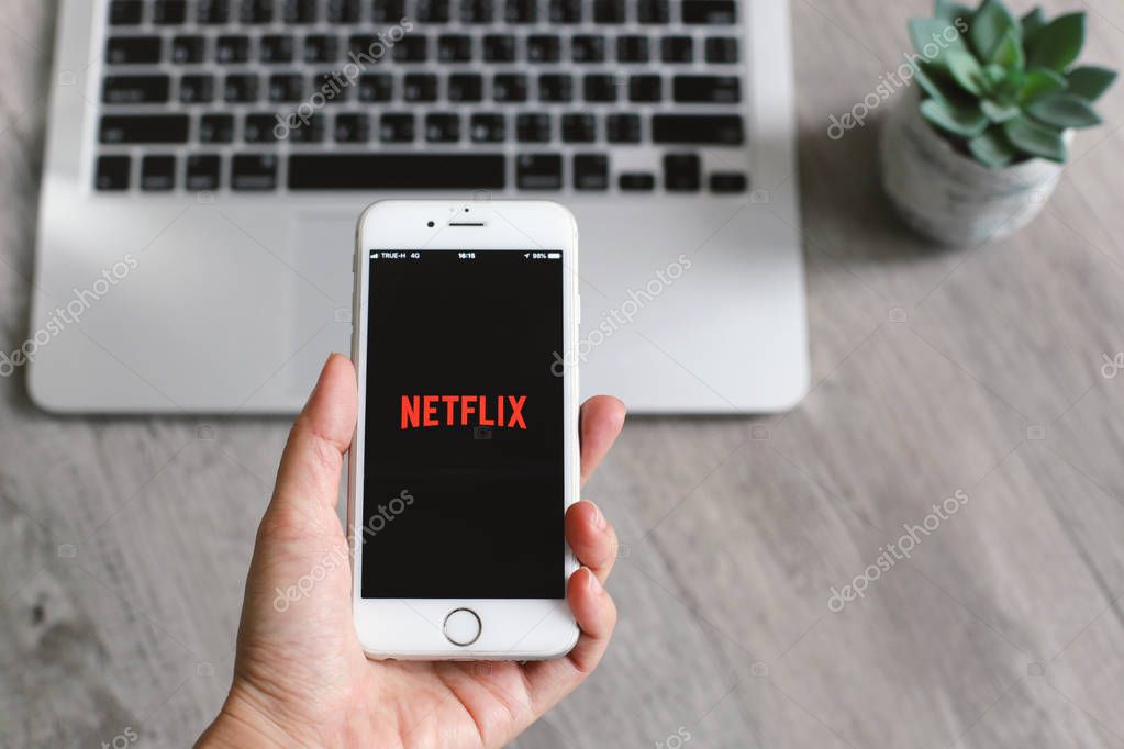 BANGKOK, THAILAND - April 28, 2018 : Close up hand holding iphone and showing Netflix app icon on screen. Netflix is an international leading subscription service for watching movies and TV series.