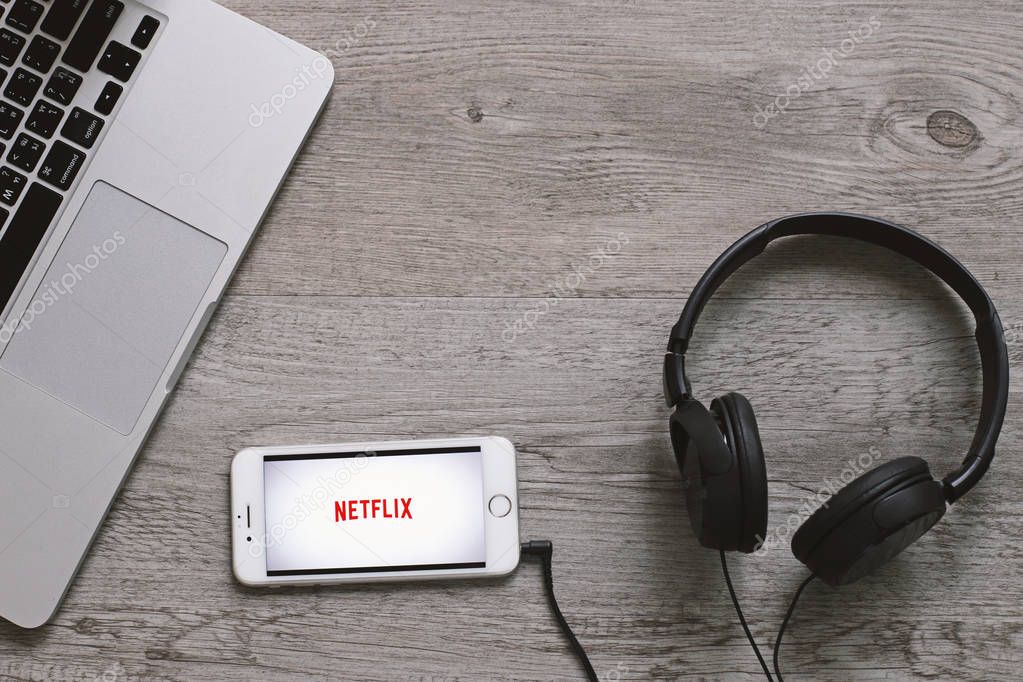 BANGKOK, THAILAND - April 28, 2018 : Top view of Netflix app icon on iphone screen with headphone and laptop. Netflix is an international leading subscription service for watching movies and TV series.