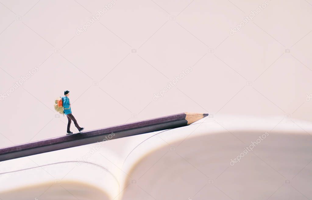 Miniature people figures with backpack walking on pencil and boo