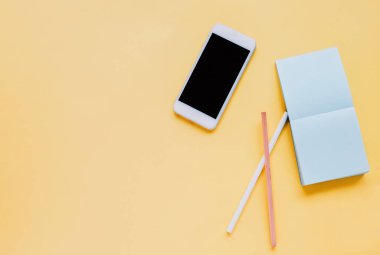 Akıllı telefonlu düz çalışma masası, parlak sarı zemin üzerine not kağıdı ve kalem.
