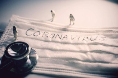 Koruyucu kıyafetli minyatür doktorlar Covid-19 ve Coronavirus salgınlarını önlüyor. Üzerinde stetoskopla yazılmış koronavirüs yazılı cerrahi maske.
