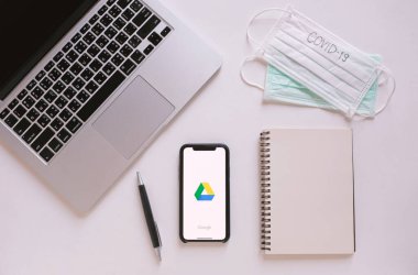 BANGKOK, THAILAND - 28 Mart 2020: Google sürücüsü uygulamasını ve dizüstü bilgisayarını gösteren akıllı telefonlu düz çalışma masası, covid-19 yazılı defter ve maskeleri, evden ve karantina konseptinden çalışma, Coronavirus 'u engelleme