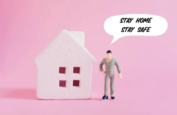Self quarantine concept, miniature toy man near house on pink background with text stay home stay safe during outbreak of COVID-19 and Coronavirus, self isolation to prevent the spread pandemic