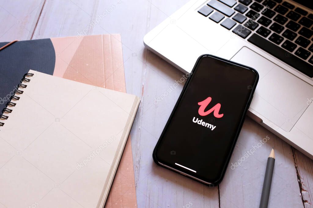 BANGKOK, Thailand - April 2, 2020 : Close up iPhone showing Udemy application and laptop with notebook. Udemy is popular online class and useful during quarantine in COVID-19 and Coronavirus
